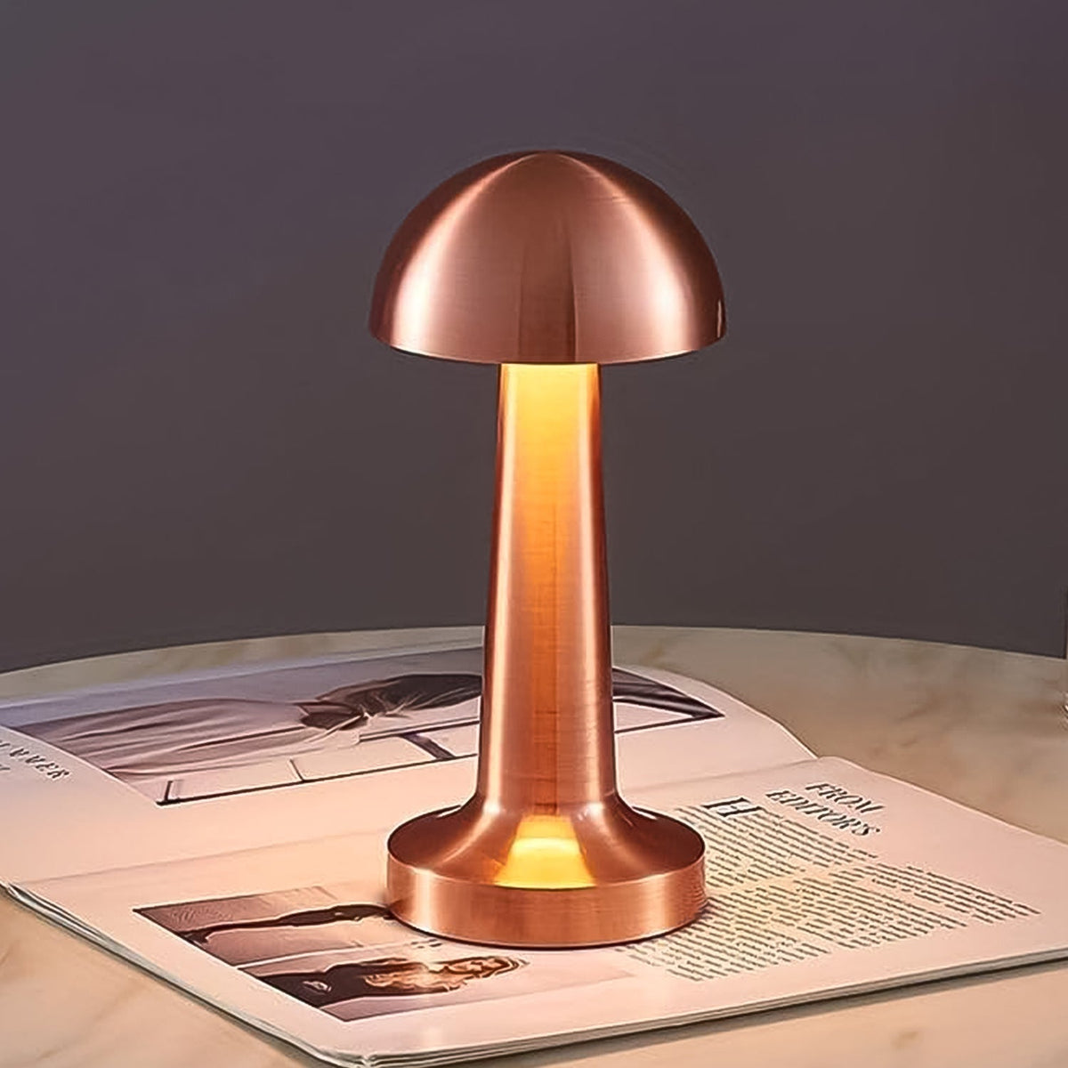 A glowing copper mushroom lamp sits on an open magazine atop a white marble table in a dim room.
