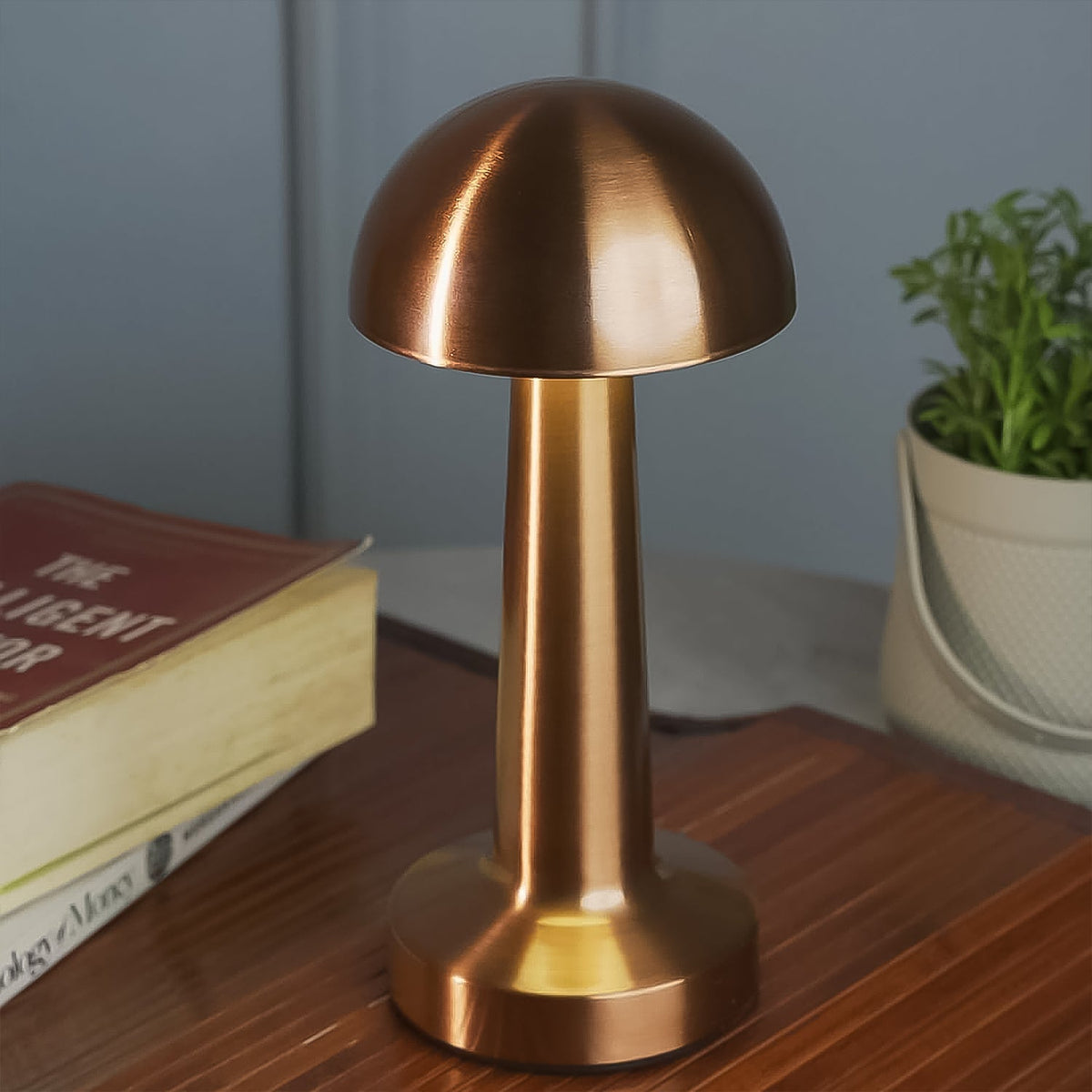 A copper mushroom lamp illuminates a wooden tray with a book and a potted plant in a soft-lit setting.