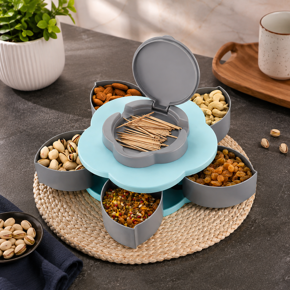 A blue and grey petal-shaped snack dispenser filled with various nuts and dried fruit, resting on a woven mat.