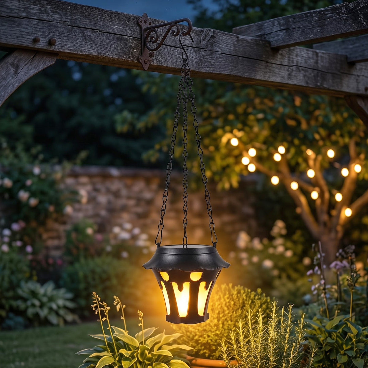 A black solar lantern with a flickering yellow light hangs from a decorative metal hook on a wooden pergola in a lush garden