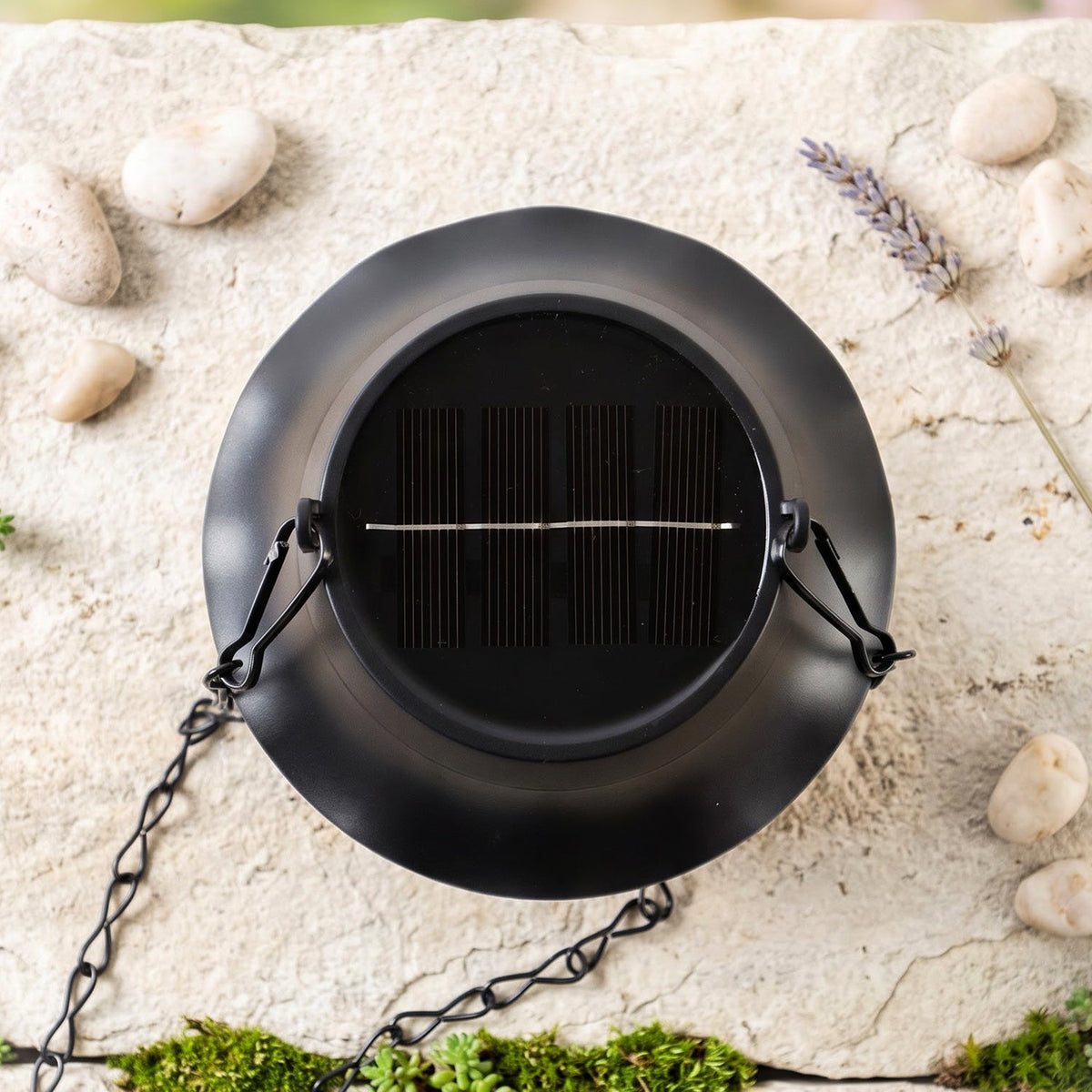 A top-down view of the black solar lantern shows its solar panel, with a chain resting on a stone surface with moss and