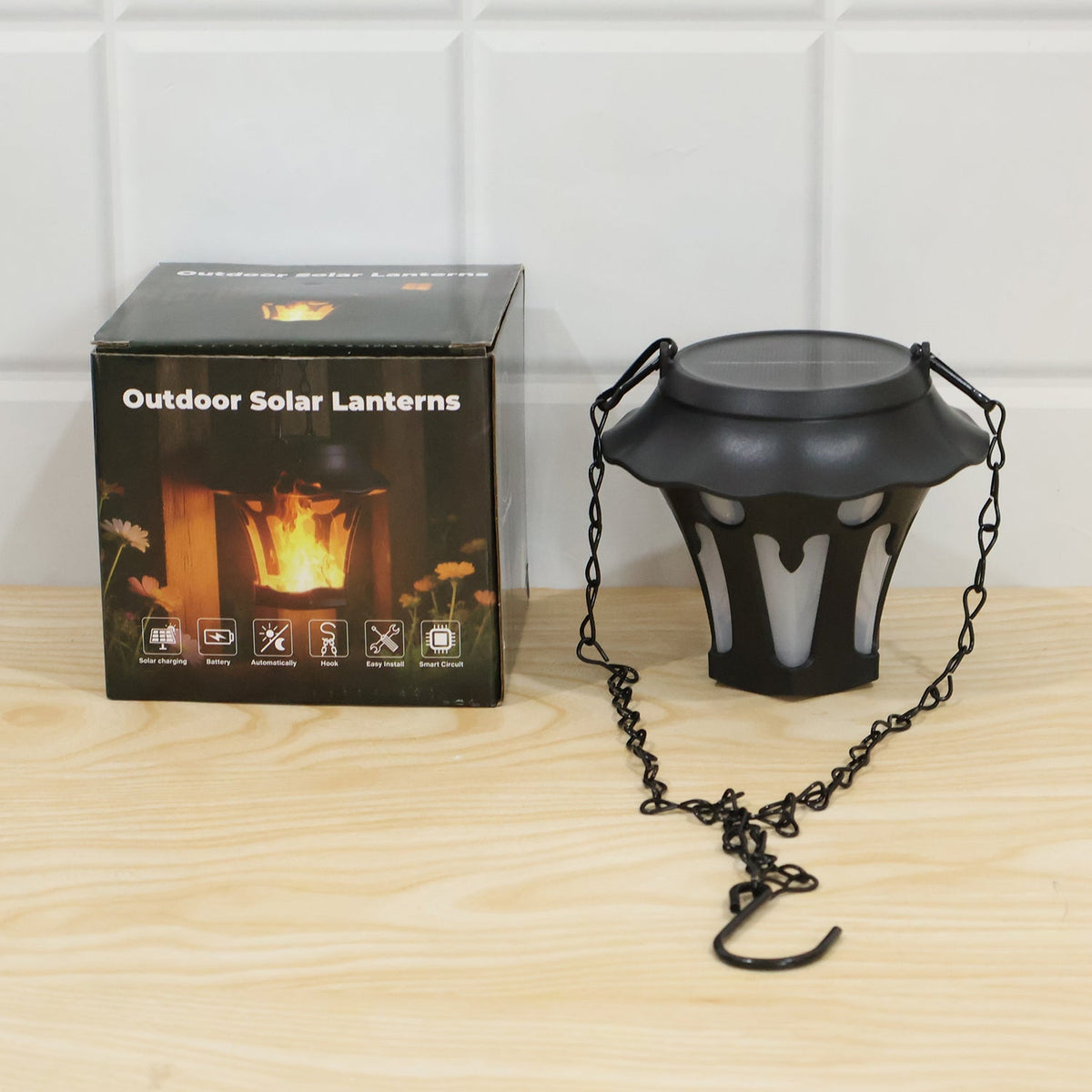 A black solar lantern with its chain and hook sits next to its black packaging box on a light wooden surface.