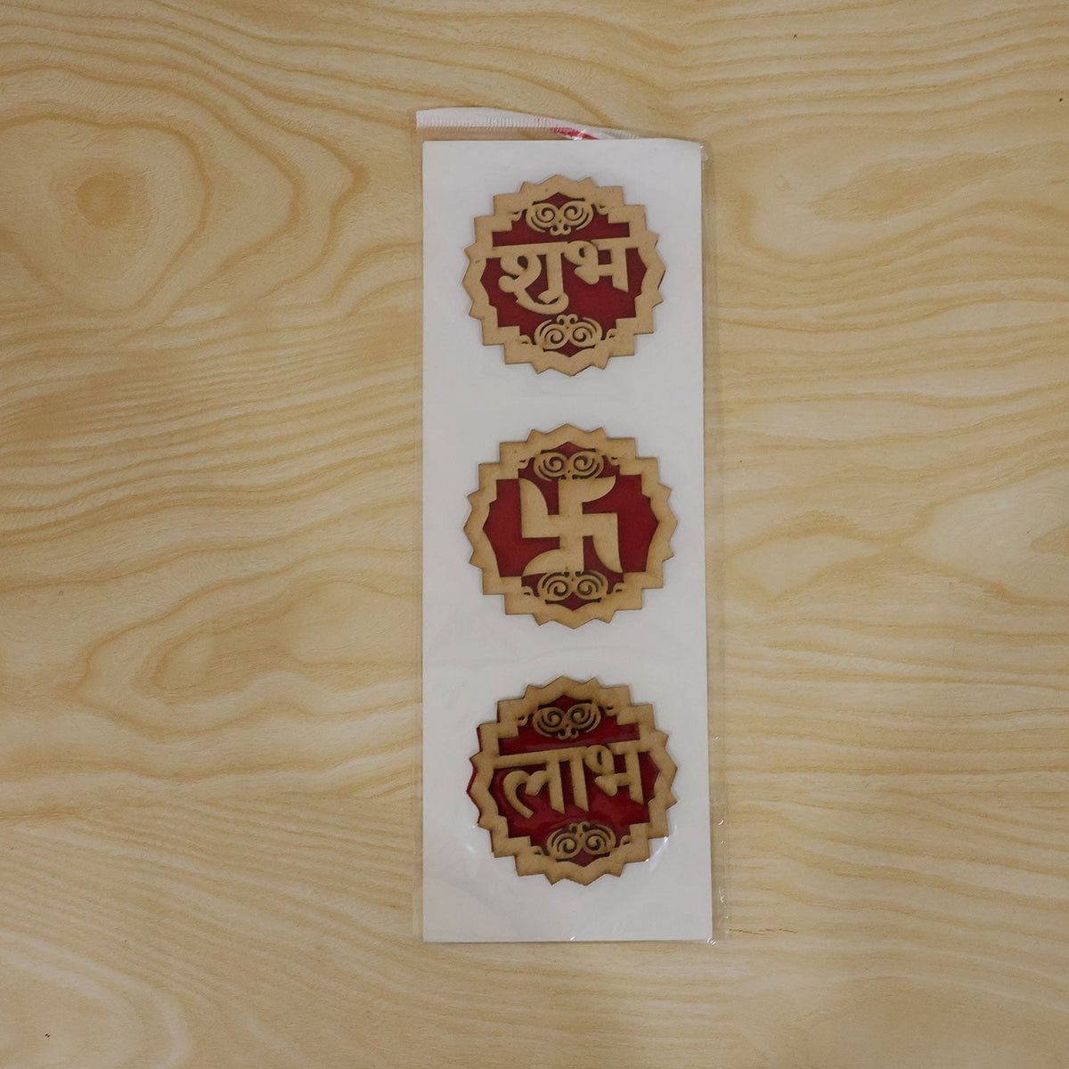 The three wooden Shubh Labh Swastik decorations are shown in clear plastic packaging on a light wooden surface.