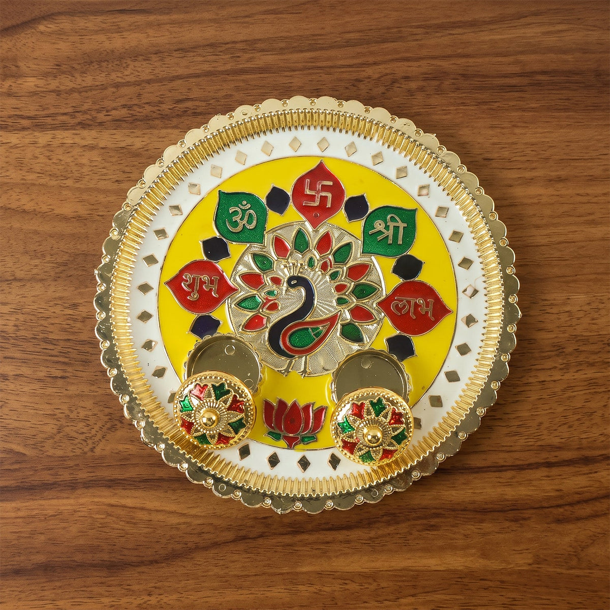A golden pooja thali with a peacock design and two empty small bowls on a wooden surface.