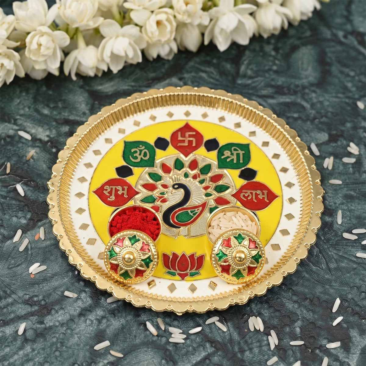 A golden and yellow pooja thali with a peacock design, two small bowls filled with powders, and scattered rice.