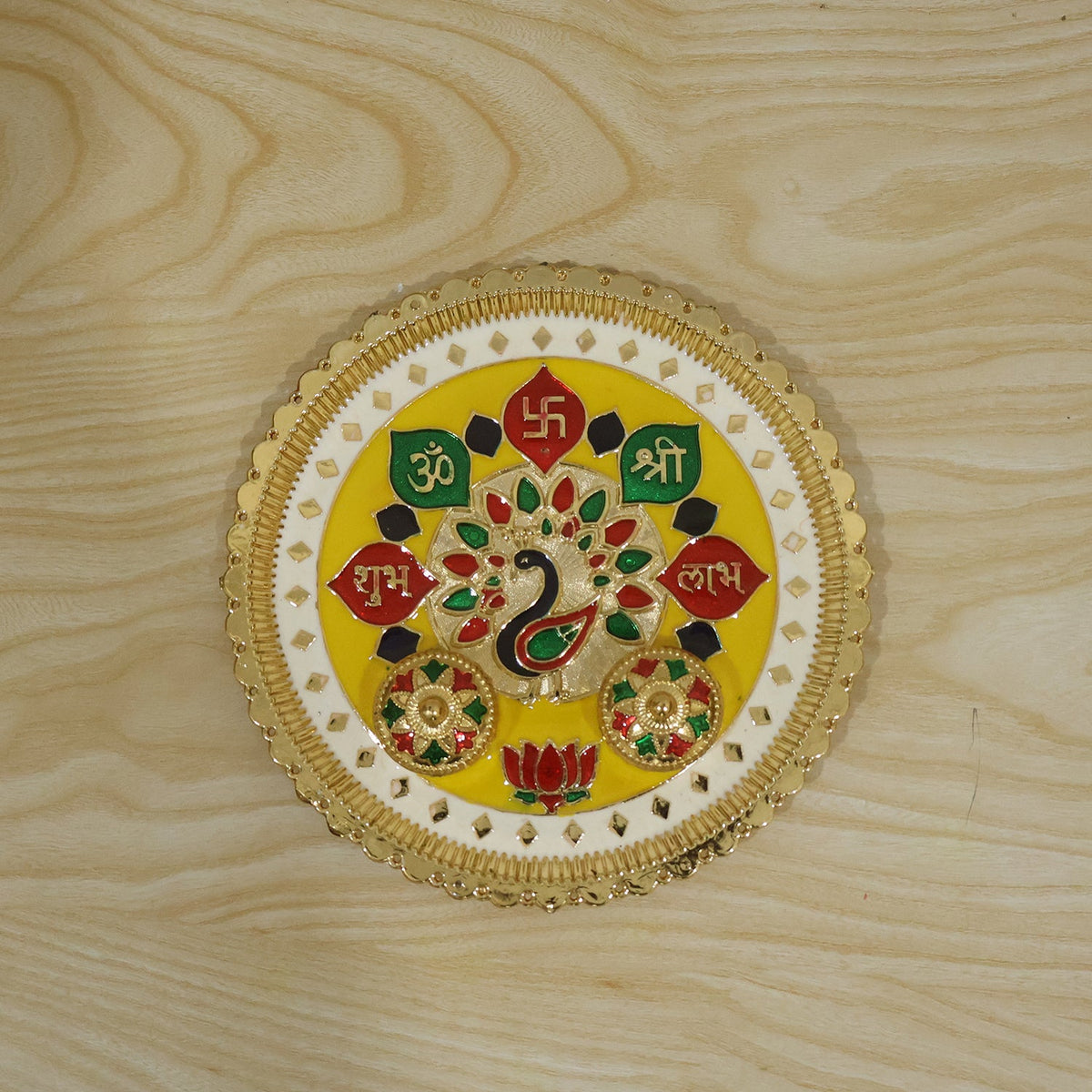 A golden pooja thali with a peacock design and two empty small bowls on a light wood surface.